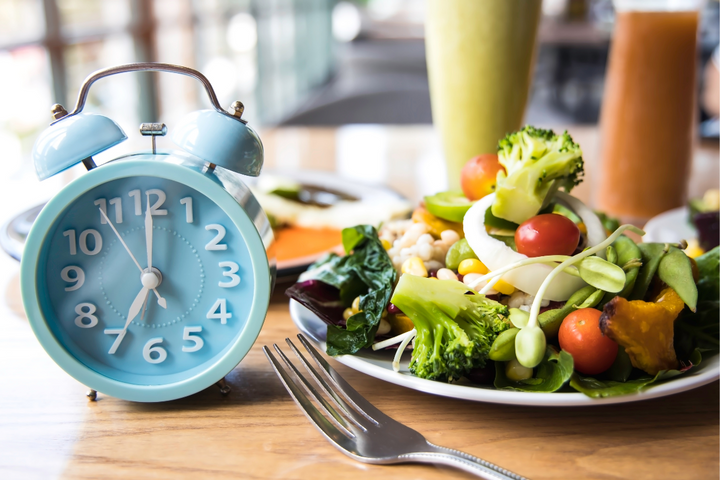 table with plated of healthy food and drinks with a clock